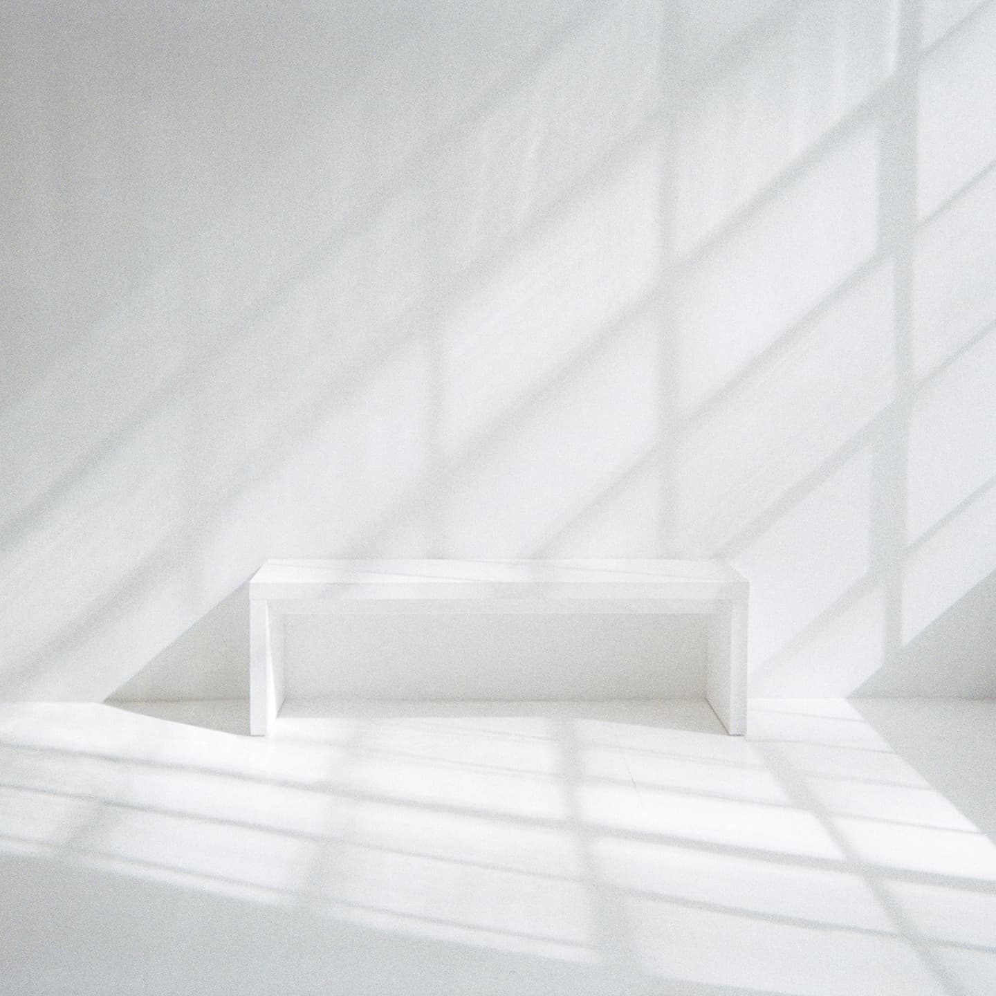 White bench in white room with sun shining against bench and wall.